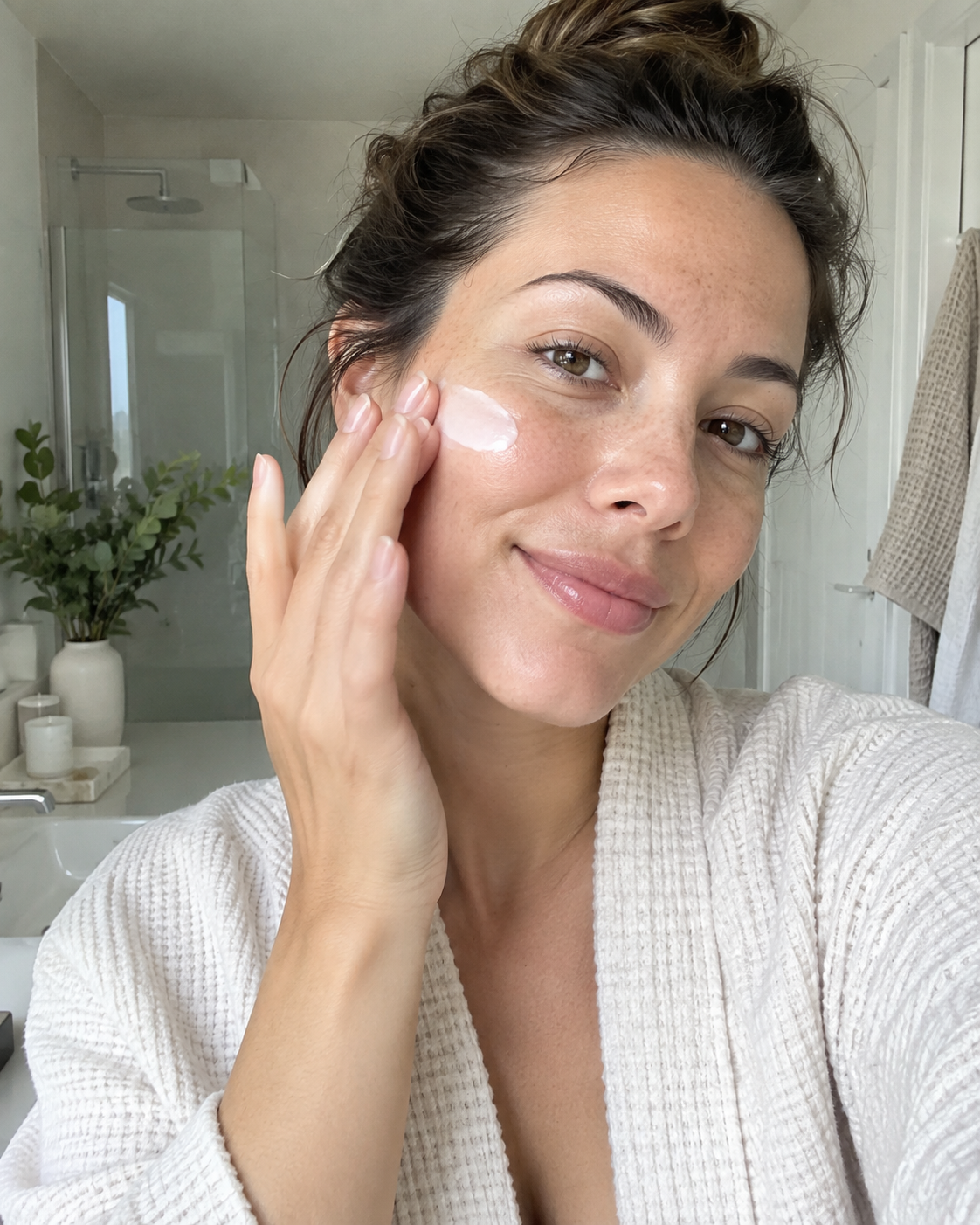 Woman applying cream to her face in a bright bathroom